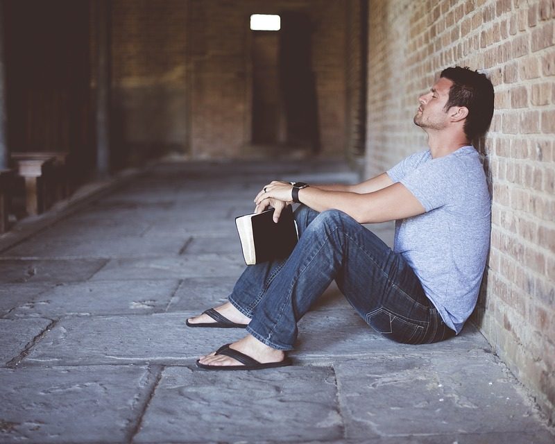 man sits alone against a brick wall